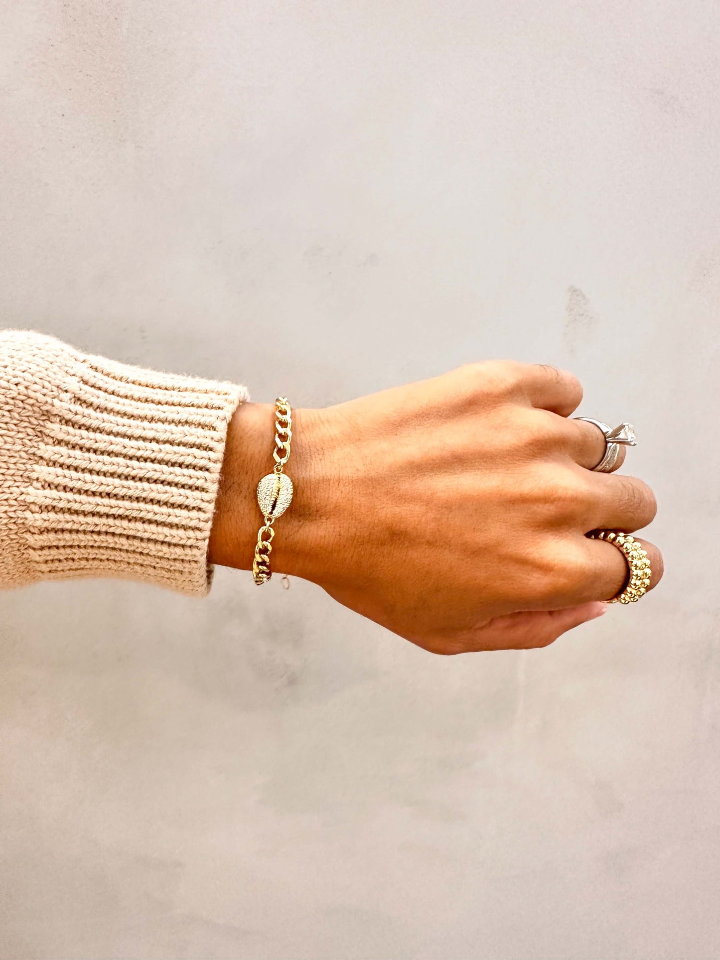 Close-up of a hand wearing the Velani Jewelry Cowrie Cuban Bracelet, showcasing gilt links and cowrie shell detail.