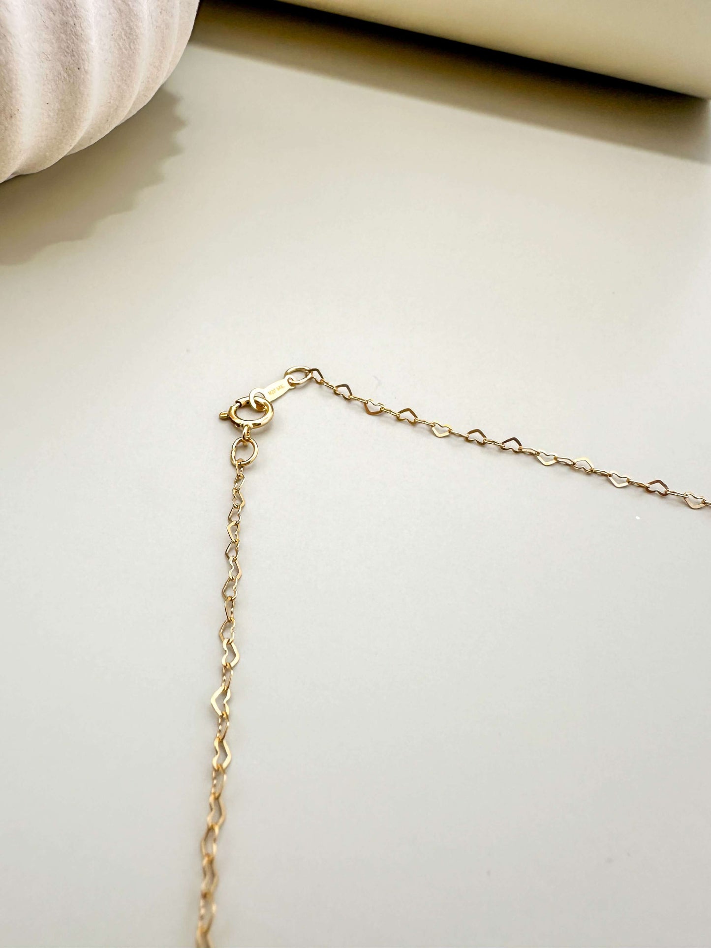 Close-up of Velani Jewelry gold filled dainty flat heart necklace chain, showing clasp details and shimmering surface.