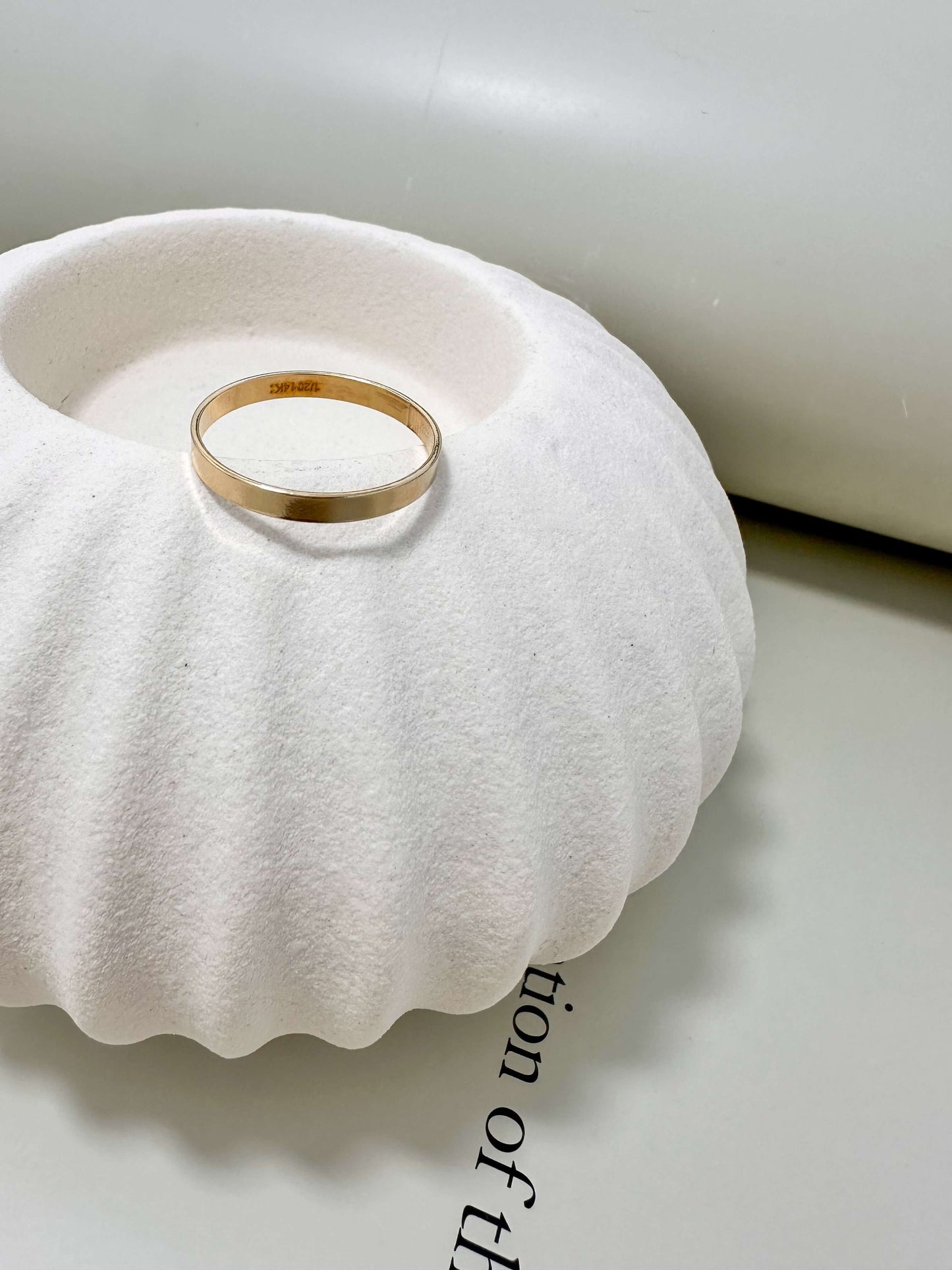 Velani Jewelry Flat Band Ring on a textured vase, showcasing its 14K Gold Filled and hypoallergenic qualities.