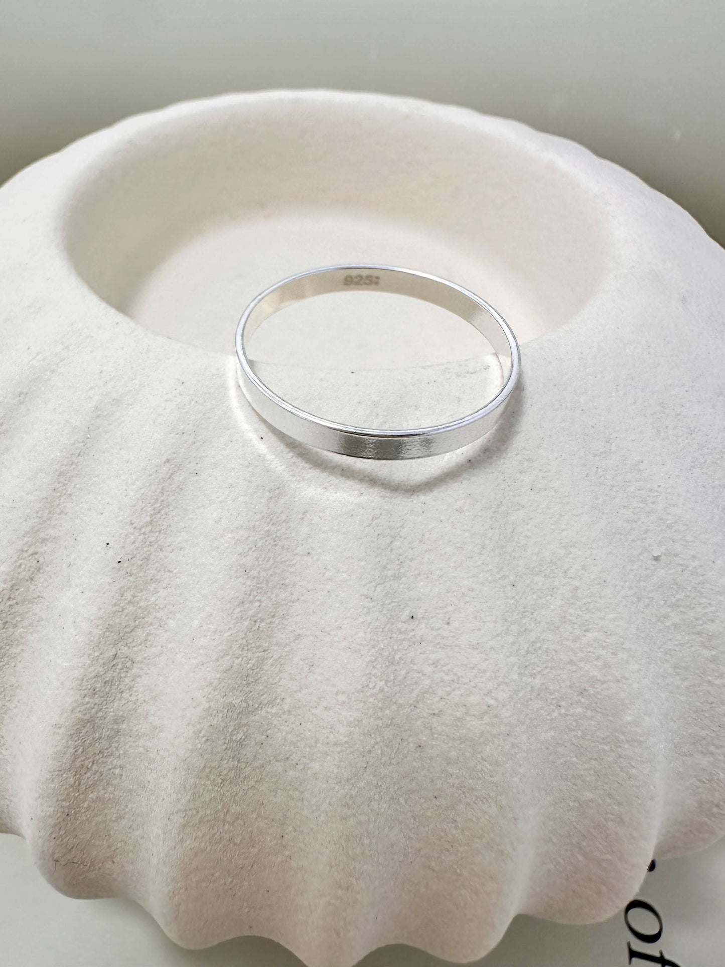Velani Jewelry Flat Band Ring on a textured shell, 14K gold filled, hypoallergenic, waterproof, and tarnish resistant.