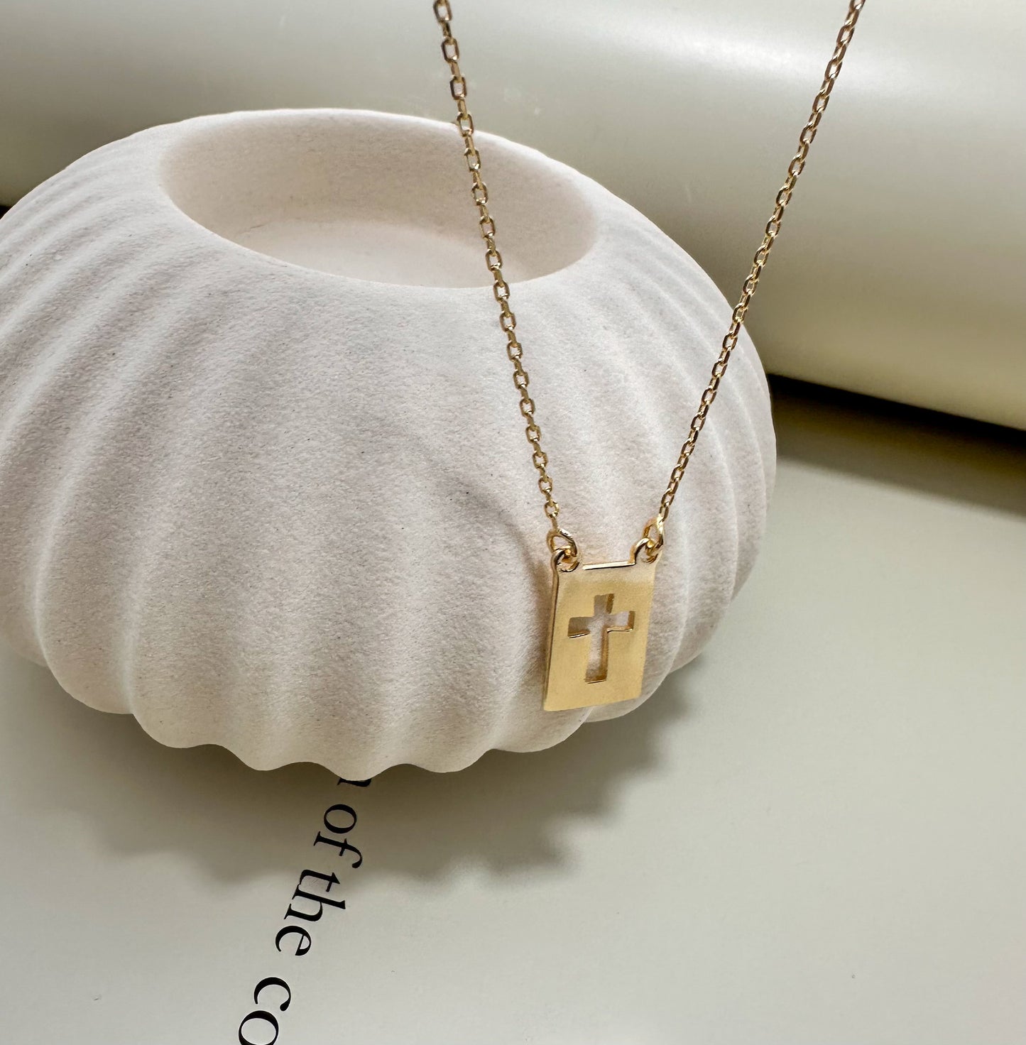 Velani Jewelry El Shaddai Cross Plaque Necklace displayed on a modern decorative bowl, showcasing its elegant design.