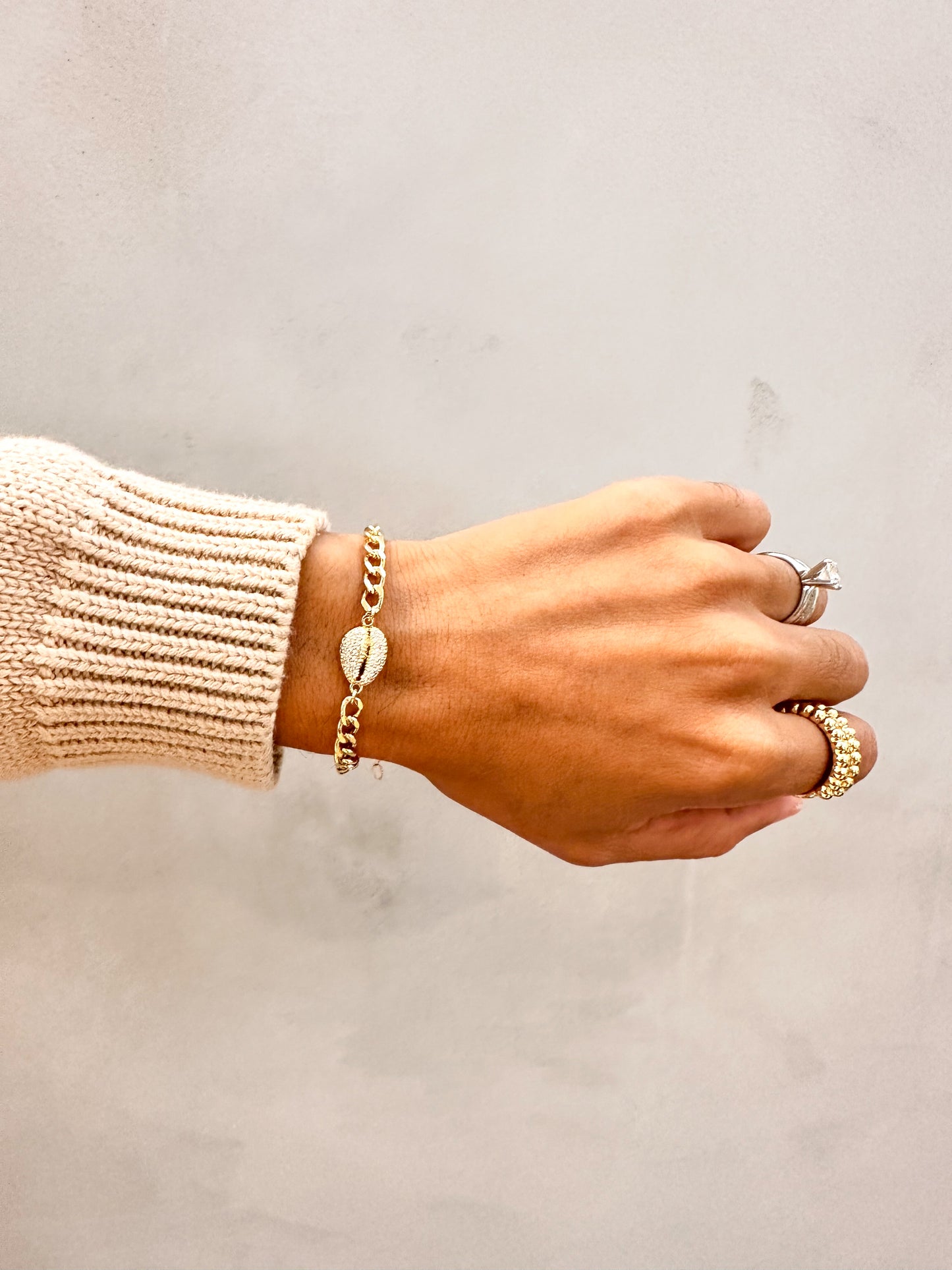 Hand wearing Velani Jewelry Cowrie Cuban Bracelet with additional rings, showcasing an elegant island style.