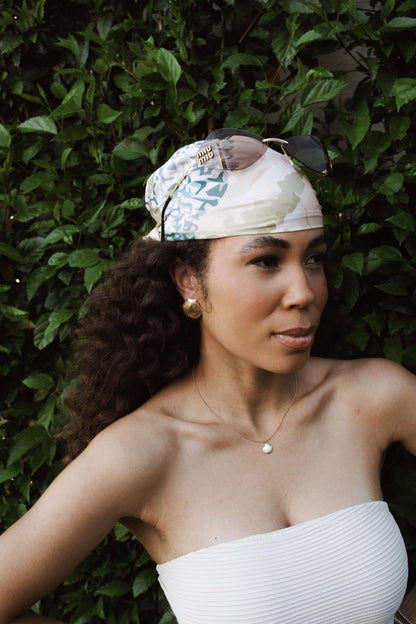 Woman wearing a patterned headscarf and sunglasses, showcasing a chic summer look among lush greenery.