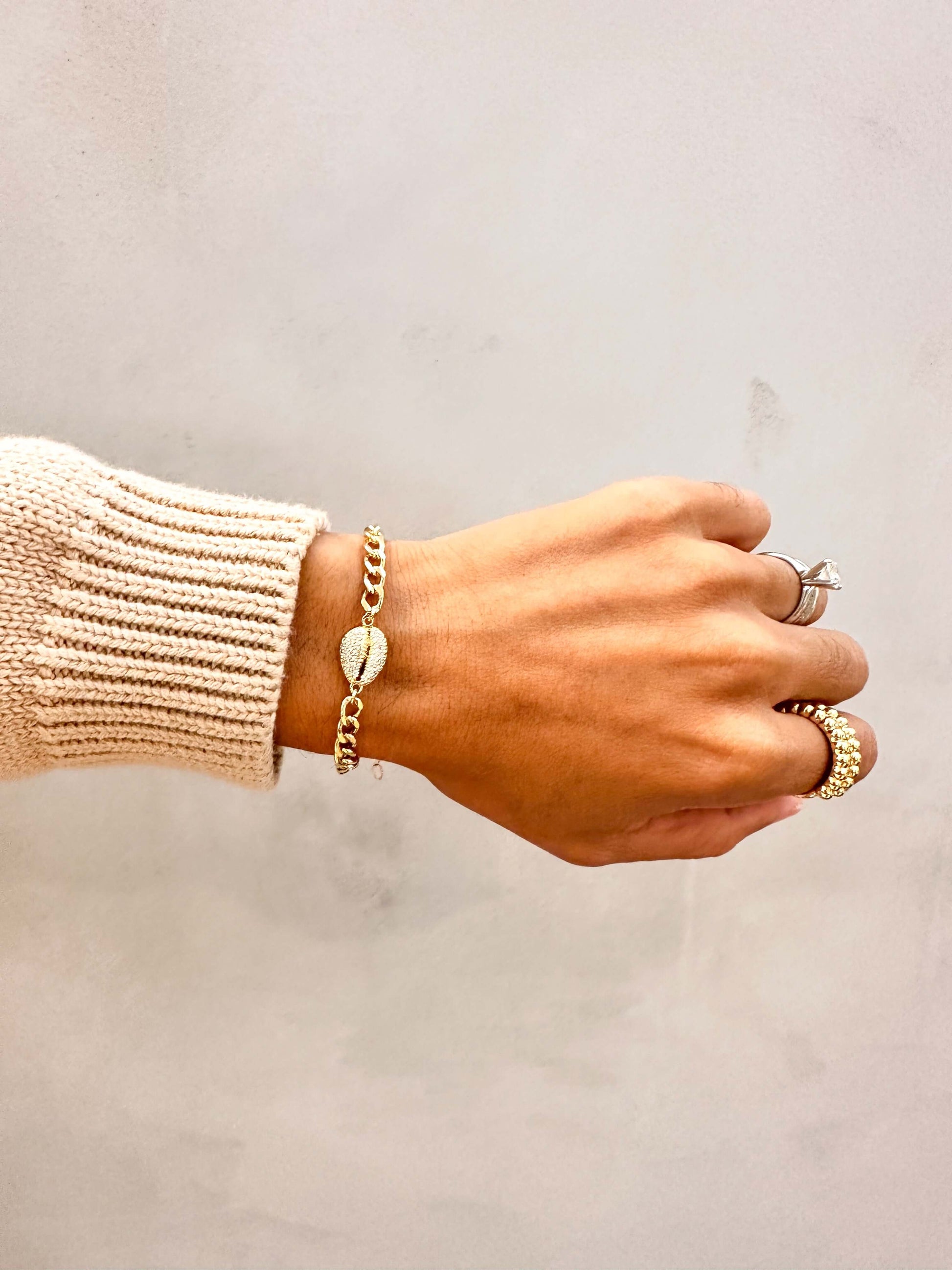 Close-up of a hand wearing the Velani Jewelry Cowrie Cuban Bracelet, showcasing gilt links and cowrie shell detail.