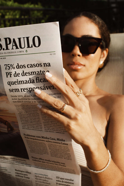 Woman wearing sunglasses reading a newspaper, showcasing a Velani Jewelry Micro Freshwater Pearl Bracelet.