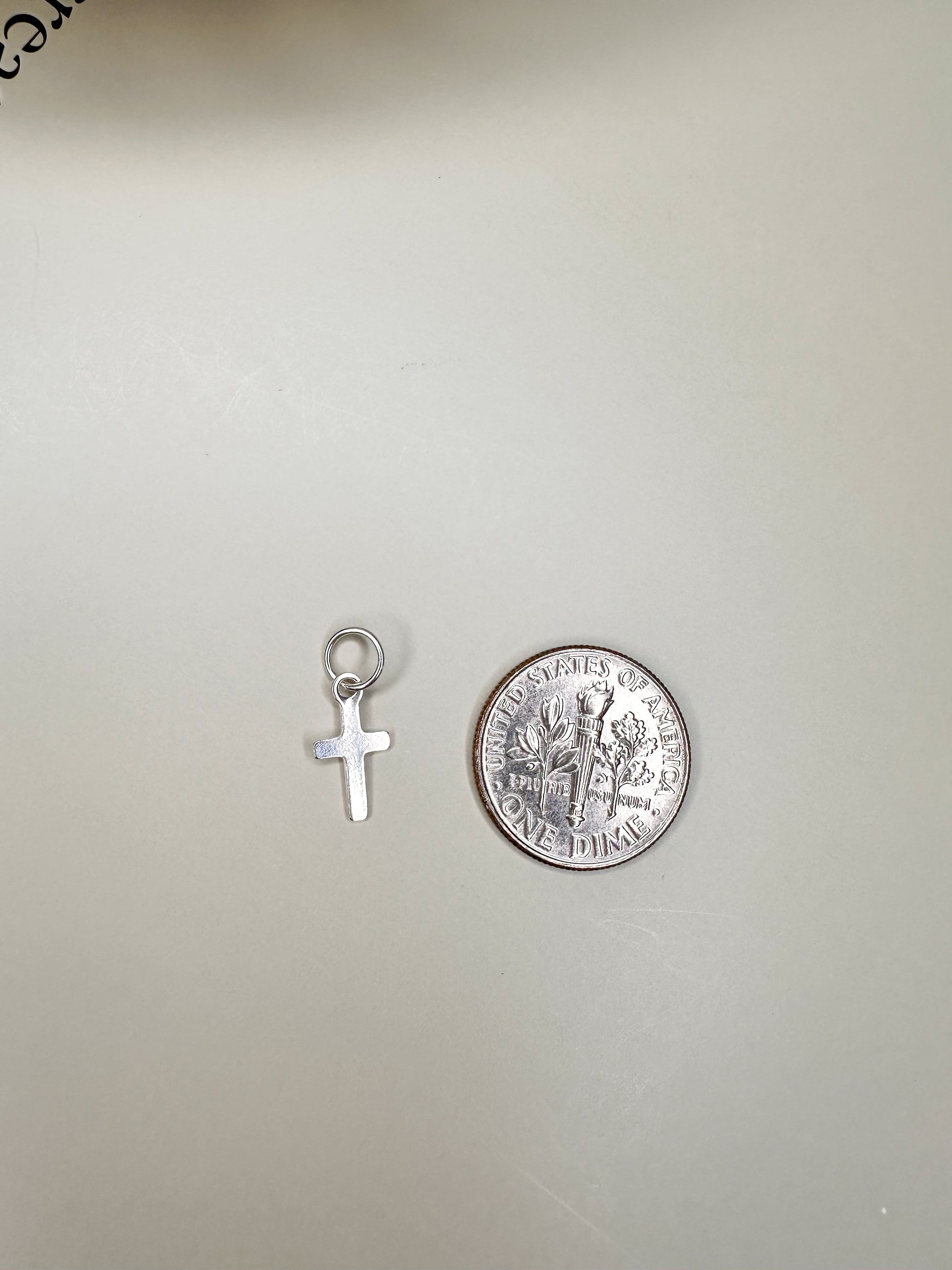 Velani Jewelry mini dainty cross pendant in sterling silver next to a coin for scale, handcrafted in Brazil, nickel-free.