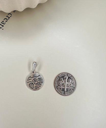 Velani Jewelry Oceans Medallion in sterling silver next to a U.S. dime, showcasing its 10mm size and handcrafted detail.