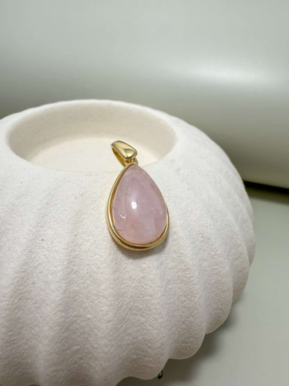 Velani Jewelry hypoallergenic gold filled teardrop pendant with rose quartz on a textured white surface.