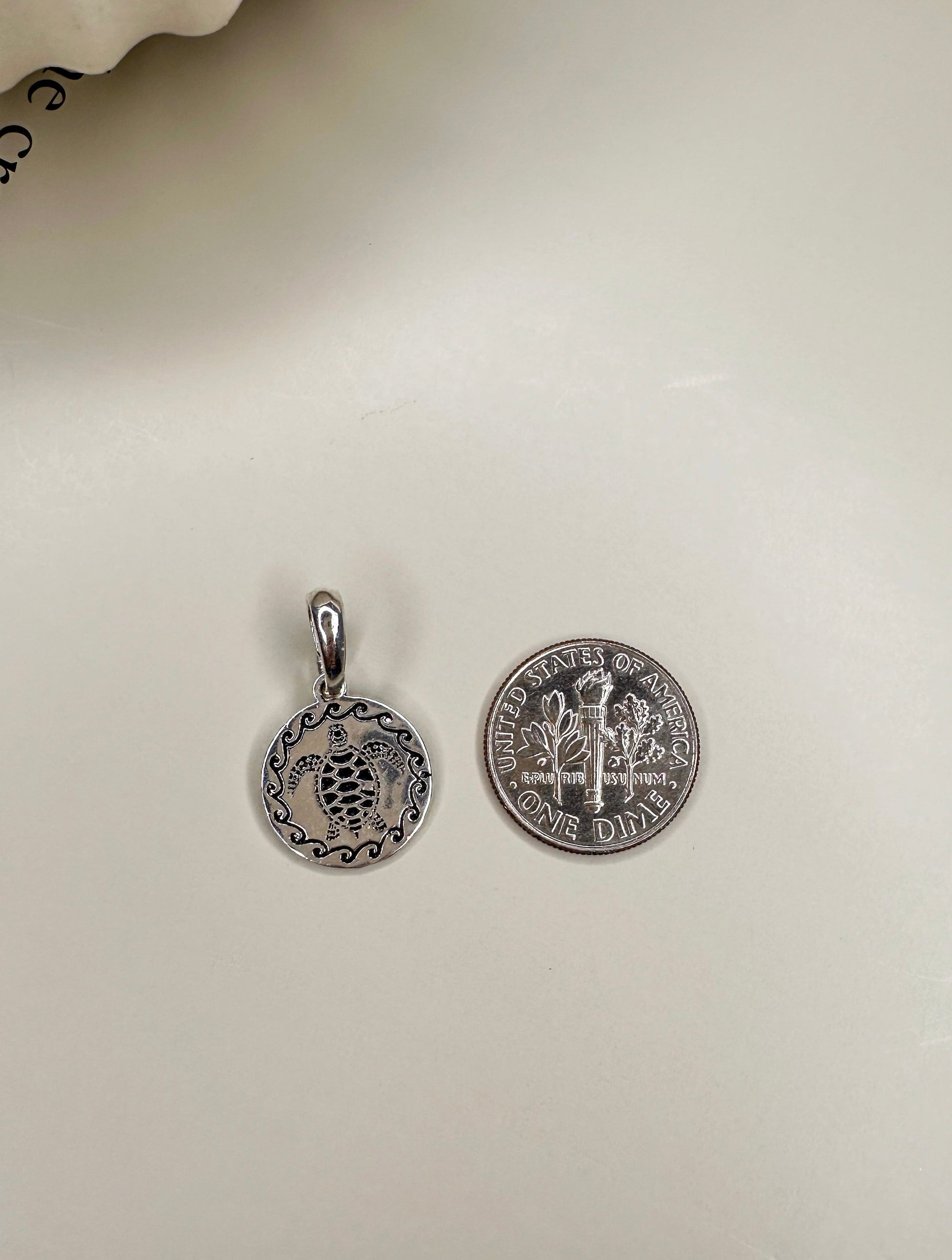 Sterling silver Velani Jewelry Turtle Medallion, 10mm, handcrafted in Brazil, shown next to a dime for size comparison.